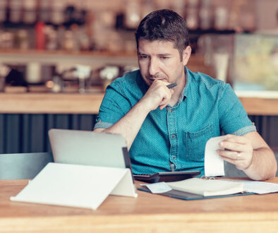 Closeup Of A Business Owner Sitting At A Table Checking Over His Business Expenses On A Tablet What Is Account Reconciliation