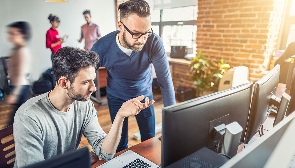 Two Website Designers Looking At A Computer Monitor Working In An Office At A Web Design Agency