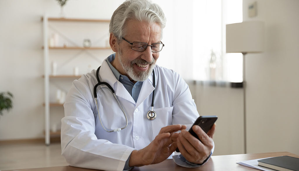 A Doctor Sitting At A Desk Smiling At A Phone In His Hands Social Media Marketing Companies