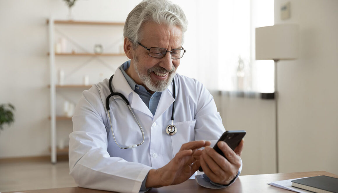 A Doctor Sitting At A Desk Smiling At A Phone In His Hands Social Media Marketing Companies