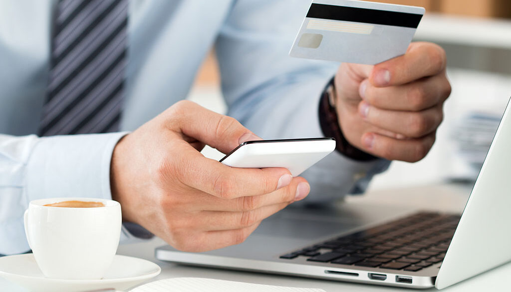 Closeup Of A Businessman Holding A Cell Phone And Credit Card In Front Of A Laptop Business Fraud Prevention