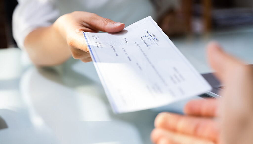 Closeup Of A Woman Handing A Paycheck To Her Employee Types Of Pay Periods