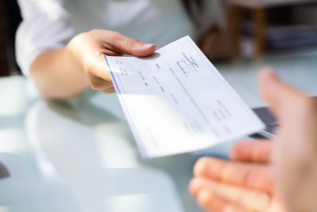 pay-period-types-explained Closeup Of A Woman Handing A Paycheck To Her Employee Types Of Pay Periods